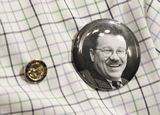A close-up shot of a shirt that has a House of Representatives pin and a button with a black-and-white photo of former Representative Rukavina on it.