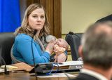 Rep. Erin Koegel feeds her baby with a bottle as she looks toward and listens to another member of the committee.