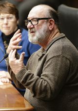 Ted Matthews sits at the testifiers' table and gestures with his hands as he speaks to someone out of view.