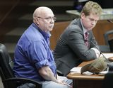 Neil Hoadley sits at the testifiers' table and speaks to someone out of view. Representative Stephenson sits beside him.