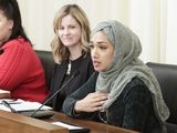 Asma Mohammed, seated at the testifier's table, speaks into the microphone to unseen committee members. Kelly Moller, seated beside her, listens to her testimony.