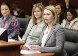 A woman, seated at the testifier's table, speaks into a microphone to committee members. Kelly Moller is seated beside her, listening to the testimony.