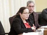 Jenny Srey sits at the testifiers' table and speaks to someone out of view. Representative Mariani sits next to her.