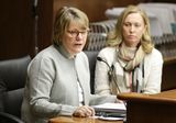 Colleen Moriarty sits at the testifiers' table and speaks to someone out of view. Representative Edelson sits next to her and watches as she speaks.