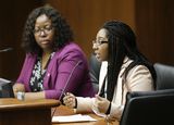 Jasmine Carey sits at the testifiers' table and speaks to someone out of view. Representative Richardson sits next to her and watches as she speaks.