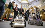 Representative Garofalo holds a controller in his hands and looks down at the robot in front of him. Alex Wicklund and Theodore Cunio give him tips on how to control the robot.