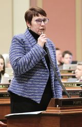 Representative Poppe stands at her desk in the House Chamber and speaks into a microphone to someone out of view.