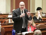 Representative Hornstein stands at his desk in the House Chamber and speaks into a microphone to someone out of view while gesturing with one hand.