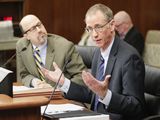 Chuck Johnson sits at the testifiers' table and speaks to someone out of view while gesturing with his hands. Representative Pinto sits next to him and watches as he speaks.