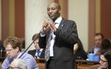 Representative Noor stands at his desk in the House Chamber and speaks into a microphone to someone out of view.