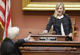 Speaker Hortman stands at the Speaker's podium and sets down a gavel with one hand and holds a different gavel in her other hand.