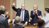 U.S. Rep. Pete Stauber waves to the members in the House Chamber. Representative Lislegard stands next to him and applauds while looking at him.