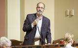 Representative Mahoney stands at his desk in the House Chamber and holds a microphone to speak to someone out of view.