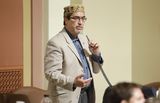 Representative Mariani stands at his desk in the House Chamber and speaks into a microphone to someone out of view.