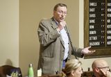 Representative Nelson stands at his desk in the Chamber and speaks into a microphone to someone out of view.