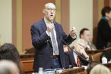 Representative Davnie stands at his desk in the House Chamber and speaks into a microphone to someone out of view while gesturing with his other hand.