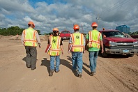 A group of workers wearing safety vests and walking on a dirt road.