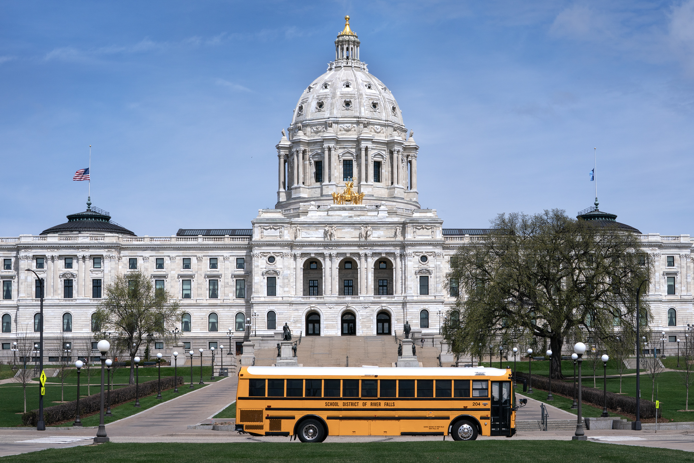 A yellow school bus parked in front of the Minnesota State Capitol on a spring day.
